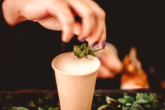 Female barista decorating coffee with mint leaves and flowers