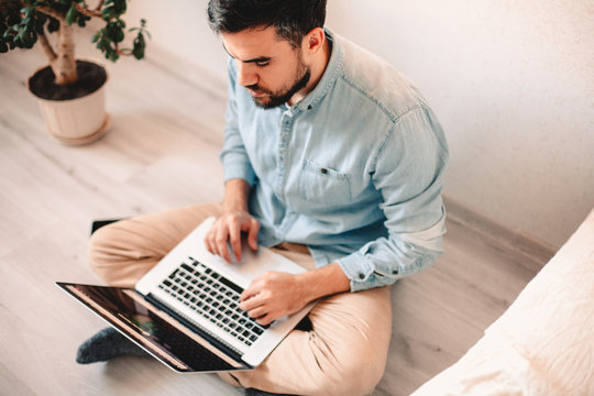 Serious man using laptop computer while sitting on floor at home