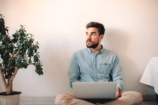 Man using laptop computer while sitting against wall on floor at home