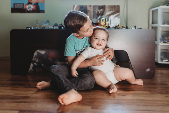 5 yr old brother holding smiling baby sister with 2 teeth on his lap