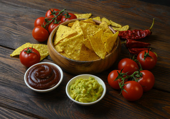 nachos in a wooden bowl and sauces on a wooden table