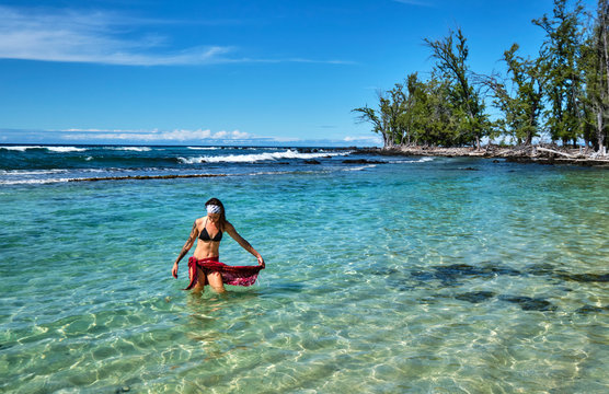 A young woman walks out of a shallow lagoon near Makalawena Beach