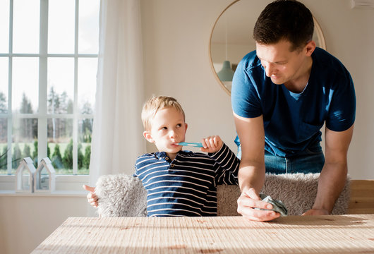 young boy brushing his teeth looking at his dad before school