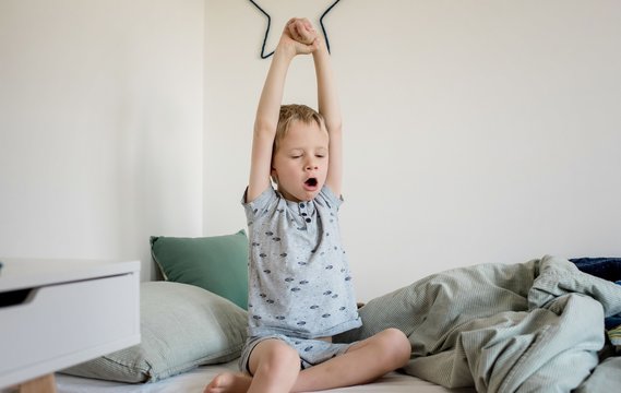 young boy waking up from a sleep and yawning in his bedroom