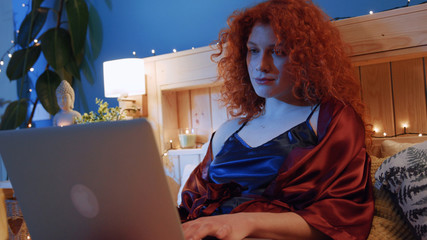 Attractive curly pretty woman use laptop on the bed at night computer evening girl social media technology touch smile happy beautiful charming close up slow motion