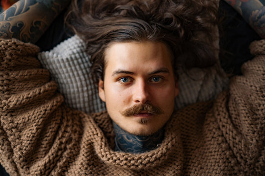 Handsome tattooed sexy man with long hair and mustache at sofa - Powered by Adobe