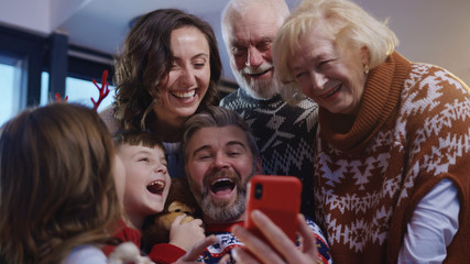 Fototapeta premium Joyful big family of three generations embrace together making a fun holiday selfie on smartphone. Full family portrait. Christmas Eve. Noel gathering.