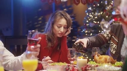 Lonely upset young woman eating food at dining table feeling lack of attention from friends on Christmas party. New Year celebration. Concept of loneliness.