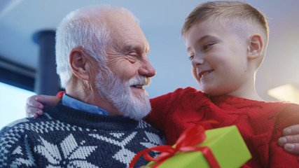 Adorable kid boy giving amazing xmas present to his cheerful grandpa on Christmas Eve. Lovely...