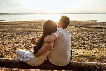 A loving couple sits on the shore, on a log and admire the golden sunset. The guy with the girl...
