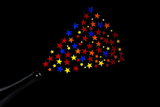 Multi-colored star confetti from a bottle of champagne. Concept for party fountain from a bottle. Black background.
