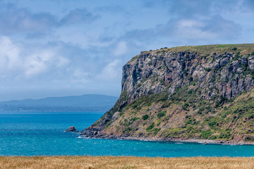 Stanley, Tasmania, Australia - December 15, 2009: Ocean side ofThe Nut volcanic plug under blue cloudscape. Deep blue water and mountains on horizon.