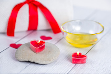 The concept of a Spa on Valentine's Day. Red heart-shaped candles, stones, massage oil and a white towel on a wooden background. Relaxation and wellness care. Bath procedure.