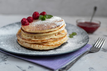 A stack of delicious pancakes with raspberries, blackberries and blueberries. On a light background. Sprinkled with icing sugar and decorated
