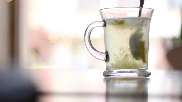 a transparent cup of hot drink, there is steam, ginger and lemon floats on a background of bokeh from the lanterns, selective focus, a hand appears and a lemon and ginger interfere with a spoon