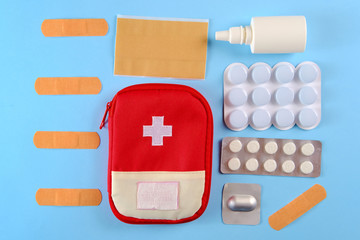 Closed tourist first aid kit pouch near to the pills, adhesive bandages and nasal spray on the bright blue background