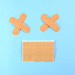 Funny smile made with brown adhesive bandages on the bright blue background