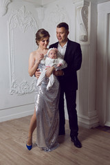 Fototapeta premium man in a black suit with a woman in a shiny long dress holding a little daughter
