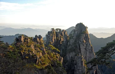 Fototapete Huang Shan Huangshan-Berg in der Provinz Anhui, China. Blick bei Sonnenaufgang vom Aussichtspunkt Dawn Pavilion mit einem Felsvorsprung und Pinien. Weite Aussicht auf Gipfel und Bäume auf dem Berg Huangshan, China.