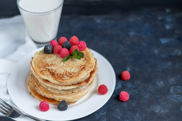 A stack of delicious pancakes with raspberries, blackberries and blueberries. On a dark stone background. Sprinkled with icing sugar and decorated