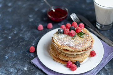 A stack of delicious pancakes with raspberries, blackberries and blueberries. On a dark stone background. Sprinkled with icing sugar and decorated