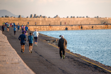 Group of people running along the promenade by the mediterranean sea at sunrise