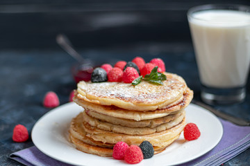 A stack of delicious pancakes with raspberries, blackberries and blueberries. On a dark stone background. Sprinkled with icing sugar and decorated