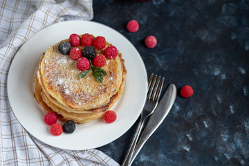 A stack of delicious pancakes with raspberries, blackberries and blueberries. On a dark stone background. Sprinkled with icing sugar and decorated