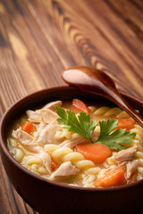 Close up of a bowl of chicken noodle soup with a wooden spoon with copy space