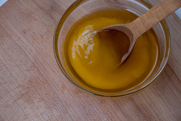 Sweet yellow honey in a glass bowl on a wooden board with a large wooden spoon. Sweet.