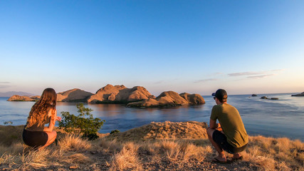 A couple standing on top of a small island, enjoying the morning sun over Komodo National Park, Flores, Indonesia. Golden hour over the islands and sea. They are enjoying their time.