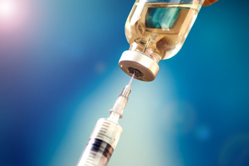 A bottle with vaccine and syringe in front of blue background. Medicine, science and healthcare...