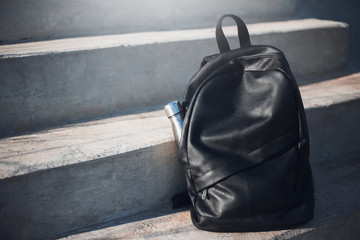 Black backpack with reusable steel thermo water bottle inside on urban stairs.