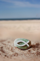 Kommunion, Konfirmation, Firmung, Taufe - weißer Fisch aus Holz auf grün bemalten Stein im Sand...