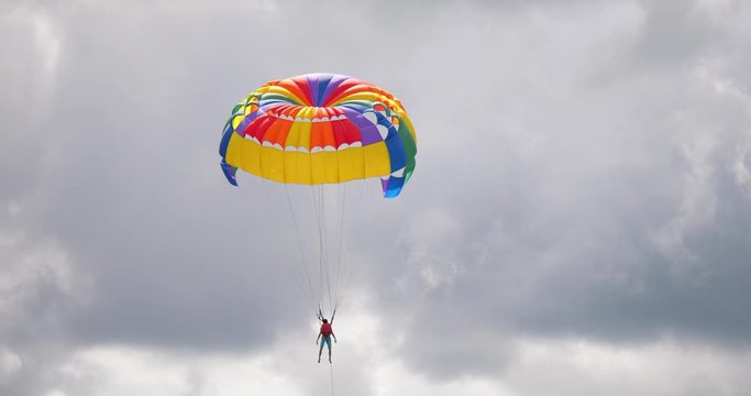 parasailor descending  with colorful parachute  parasaling parachute moving in the sky tourist parasaling in sunny day