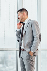 Handsome man weared in gray suit and tie, having phone talk, looks decisively, isolated over white background