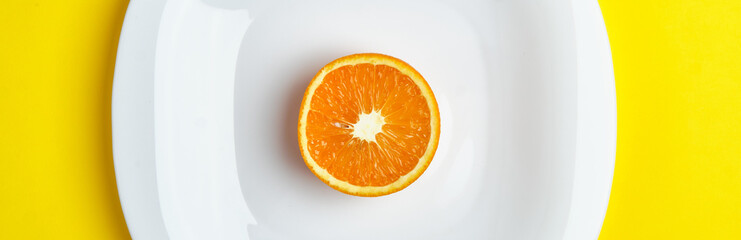 Top view of the half of the orange at the white dish lies on the bright yellow background. Healthy food, detox, diet concept