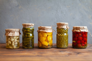 Pickled patissons, cucumbers, mushrooms, green pea and tomatoes canned into glass jars. Ingredients for vegetables preserving. Healthy fermented food concept. Harvest storing. Fermented vegetables