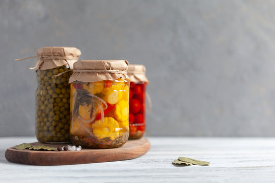 Pickled patissons, cucumbers, mushrooms, green pea and tomatoes canned into glass jars. Black background. Ingredients for vegetables preserving. Healthy fermented food concept. Fermented vegetables