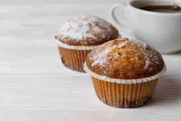 Freshly baked homemade muffins with sugar powder and a cup of coffee. Close up background