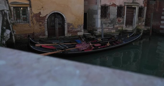 Two traditional Venetian rowing boats, gondolas, floating in the narrow channel surrounded by old colorful desolate houses. Revealing high angle shot from the bridge.