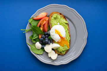 Wholesome tasty full of vitamins and health breakfast with avocado, berries, cheese and tomatoes with basil.