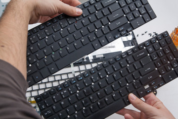 A laptop repairman is holding an old and new keyboard in his hands. Keyboard replacement in a laptop