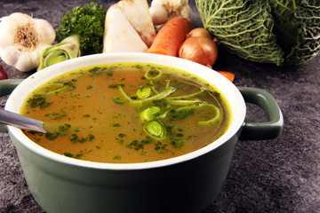 Broth with carrots, onions various fresh vegetables in a pot - colorful fresh clear spring soup. Rural kitchen scenery vegetarian bouillon stock