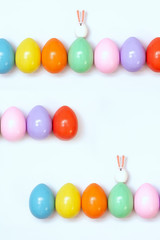 Top view of an Easter composition of painted eggs in bright juicy colors on a white background with two little rabbits. Holiday concept, flat layout, minimalism