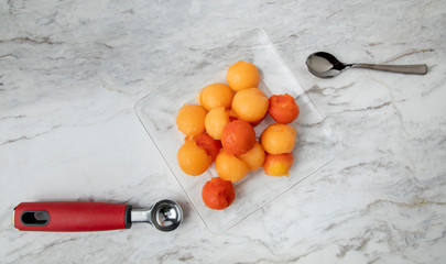 Fruta en un plato de cristal, sobre una barra de mármol blanco con una cuchara y el cortador