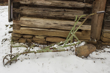 Old rusty plough in snow and wooden cabin