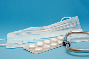 Medical mask, white tablets, phonendoscope on a blue background with a copy space