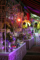 A sweet table with desserts and sweets in purple colors. Cake in pink colors on a glass stand, cupcakes, marshmallows surrounded by flowers. Decor luxury wedding celebration.