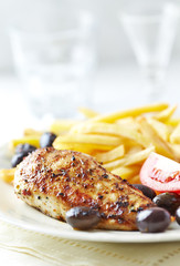 Spicy chicken breast with french fries, black olives and tomatoes. Close up.